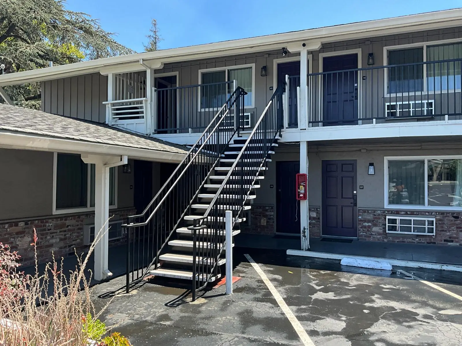 Two-story motel exterior with outdoor black metal stairs leading to upper-floor rooms and parking spaces.